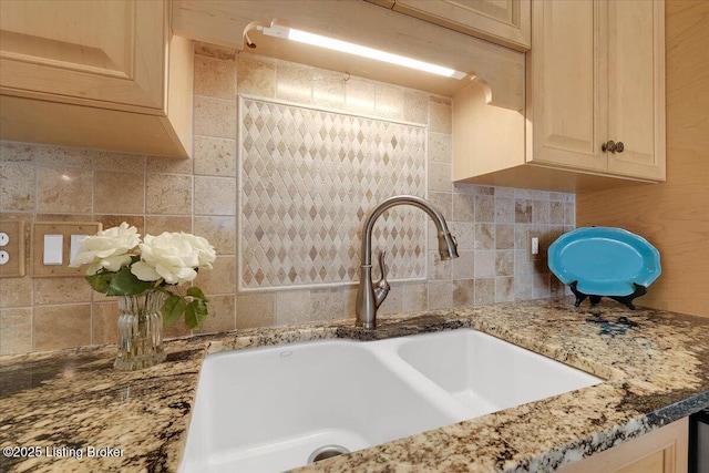 kitchen with light stone counters, decorative backsplash, and a sink