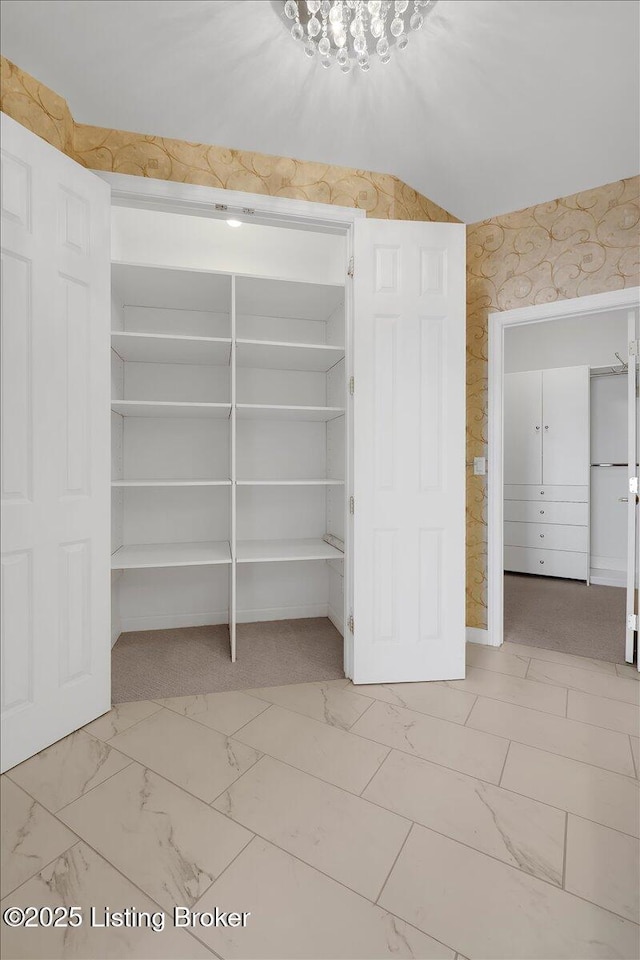 interior space featuring lofted ceiling, marble finish floor, and wallpapered walls