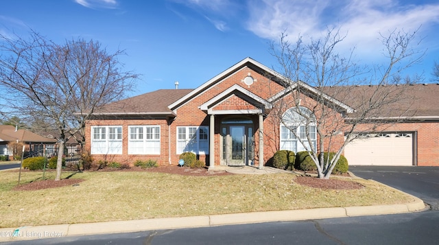 ranch-style house with aphalt driveway, an attached garage, a shingled roof, brick siding, and a front yard