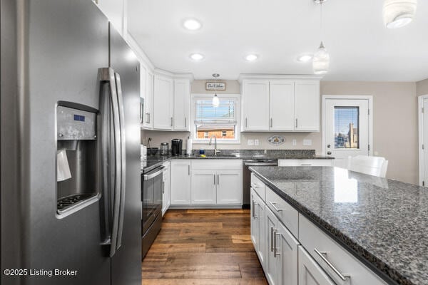 kitchen featuring white cabinetry, dark stone countertops, appliances with stainless steel finishes, dark hardwood / wood-style floors, and pendant lighting