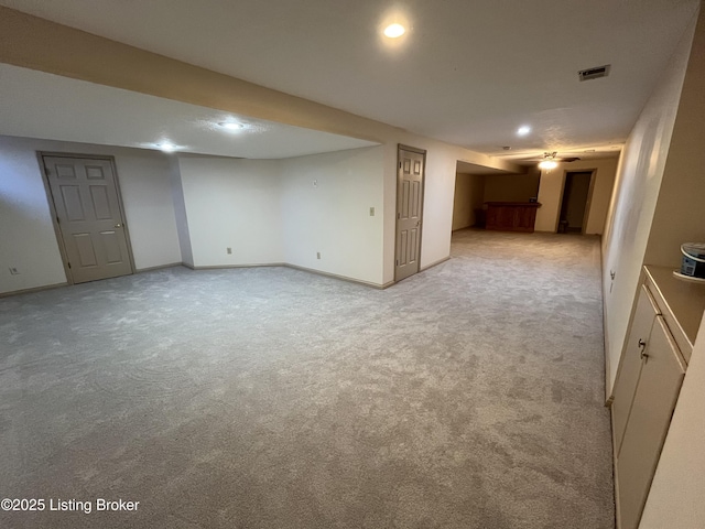 basement with ceiling fan and light colored carpet