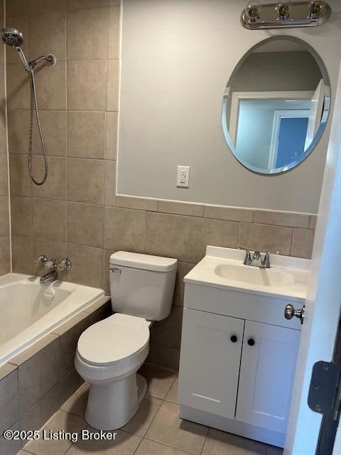 full bathroom with toilet, tiled shower / bath, tile walls, vanity, and tile patterned flooring