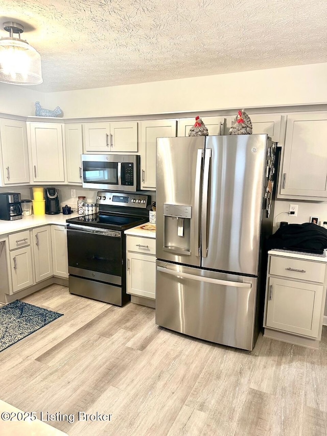 kitchen with appliances with stainless steel finishes, light hardwood / wood-style flooring, and a textured ceiling