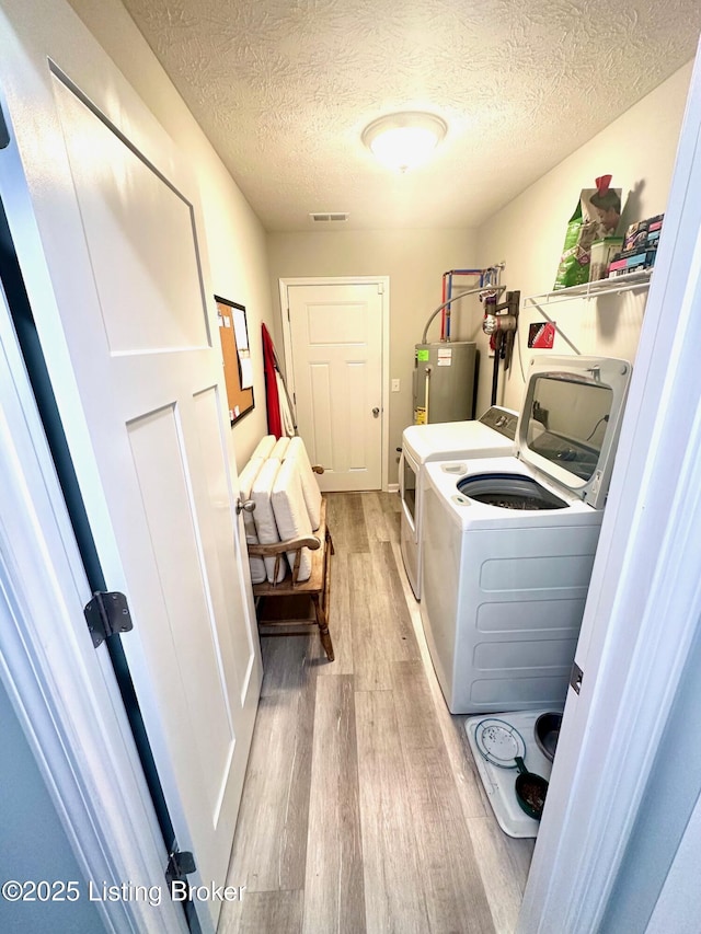 clothes washing area with water heater, light hardwood / wood-style flooring, washer and dryer, and a textured ceiling