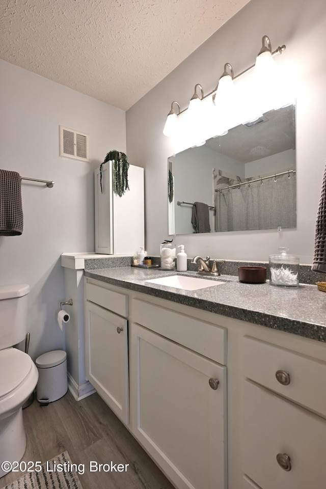 bathroom featuring hardwood / wood-style flooring, a shower with shower curtain, vanity, a textured ceiling, and toilet