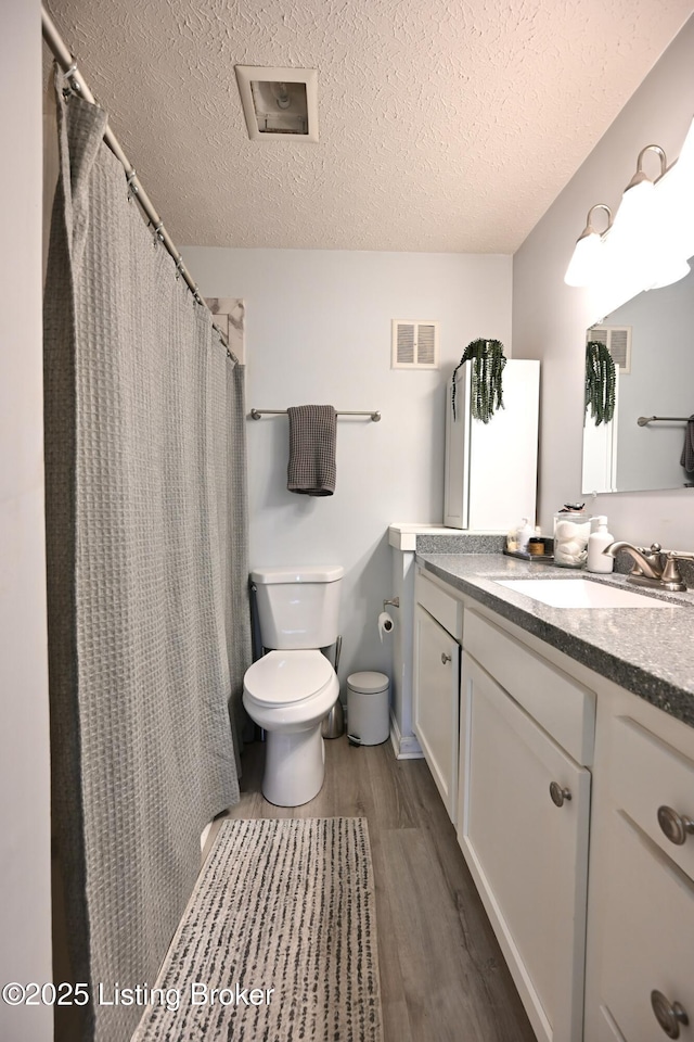 bathroom featuring wood-type flooring, vanity, a textured ceiling, and toilet