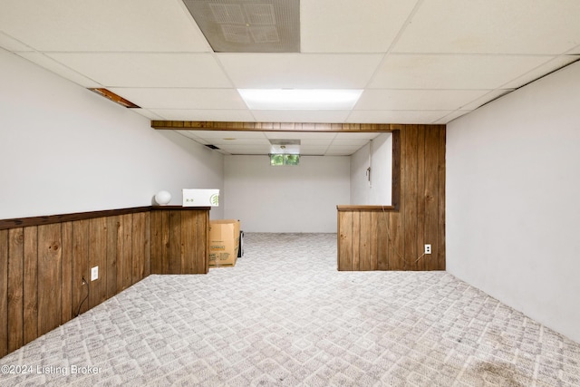 basement featuring carpet flooring, wooden walls, and a paneled ceiling