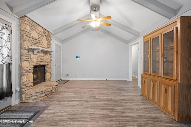 unfurnished living room featuring ceiling fan, wood-type flooring, a stone fireplace, and lofted ceiling with beams