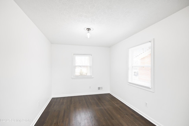 spare room with a textured ceiling and dark hardwood / wood-style flooring