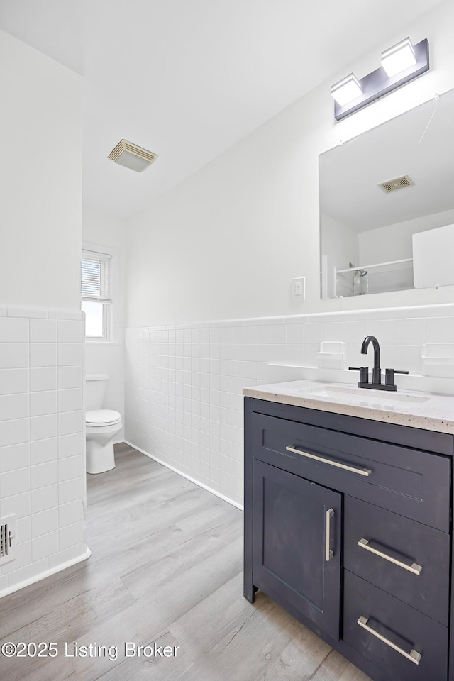 bathroom with tile walls, hardwood / wood-style floors, vanity, and toilet