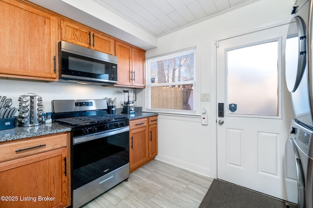 kitchen with stacked washing maching and dryer, appliances with stainless steel finishes, ornamental molding, and dark stone counters