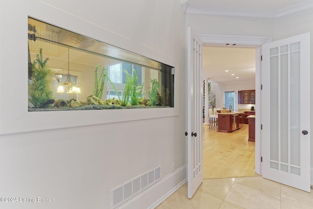 hall featuring tile patterned flooring, crown molding, and an inviting chandelier