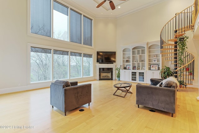 living room featuring a high ceiling, ornamental molding, ceiling fan, and light hardwood / wood-style flooring