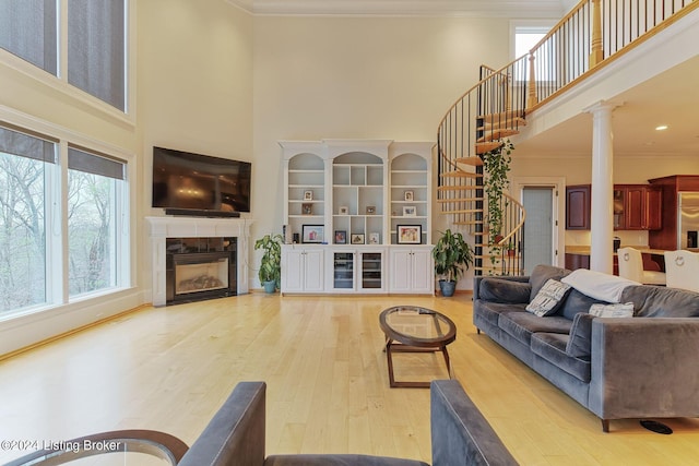 living room featuring hardwood / wood-style flooring, ornamental molding, a towering ceiling, and ornate columns