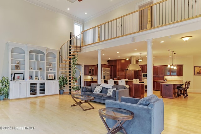 living room with ornate columns, ornamental molding, a high ceiling, and light wood-type flooring