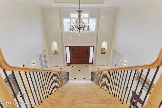 staircase with a towering ceiling, ornamental molding, and a chandelier