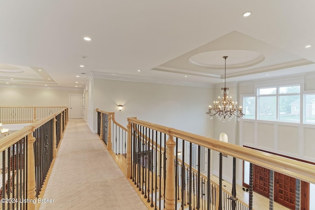 hall with light colored carpet, ornamental molding, a raised ceiling, and a chandelier