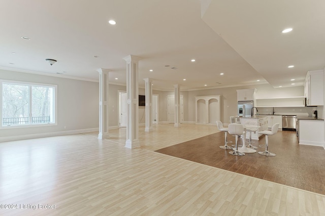 living room with ornate columns, crown molding, and light wood-type flooring