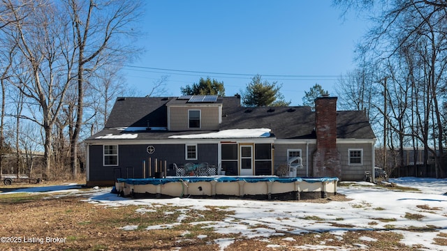 snow covered rear of property with a covered pool, a sunroom, and solar panels