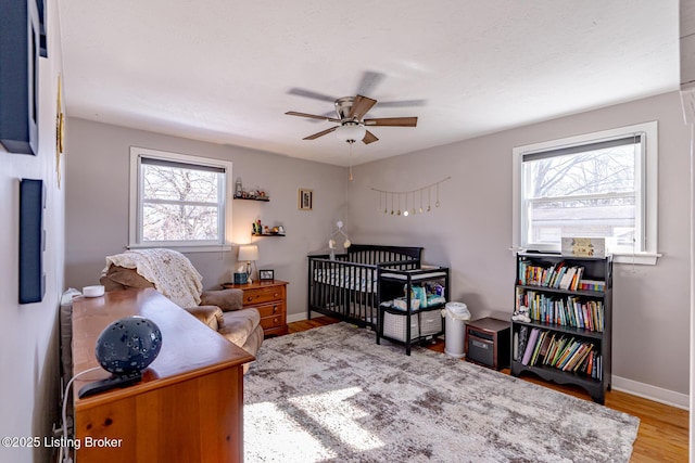 bedroom featuring a nursery area, ceiling fan, and wood-type flooring