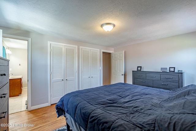 bedroom featuring multiple closets, connected bathroom, a textured ceiling, and light hardwood / wood-style floors