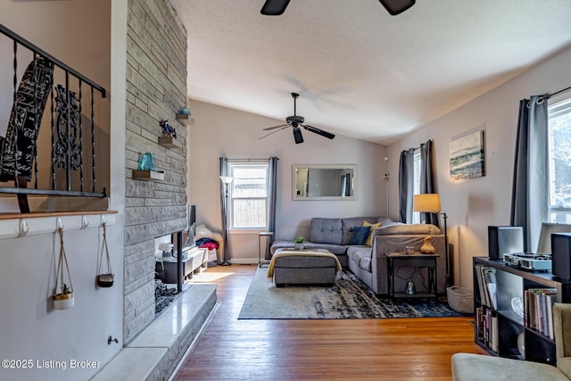 living room with light hardwood / wood-style flooring, ceiling fan, a fireplace, a textured ceiling, and vaulted ceiling