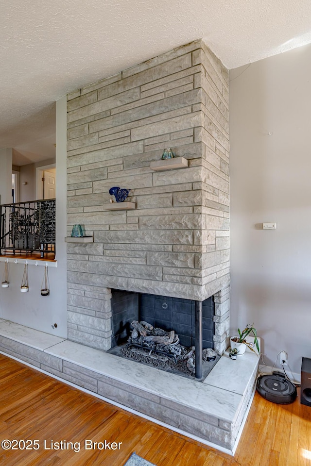 room details with hardwood / wood-style flooring, a stone fireplace, and a textured ceiling