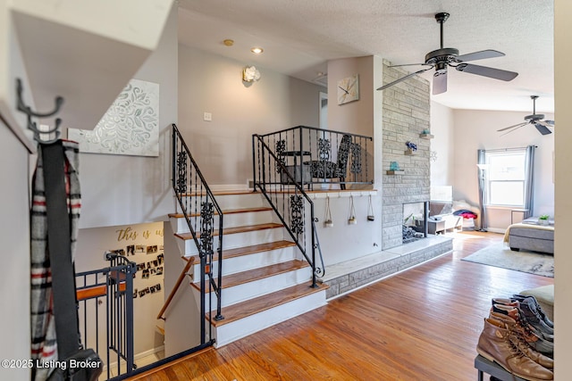 staircase featuring lofted ceiling, a textured ceiling, ceiling fan, a fireplace, and hardwood / wood-style floors