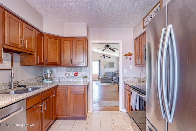 kitchen featuring sink, light tile patterned floors, ceiling fan, stainless steel appliances, and light stone countertops