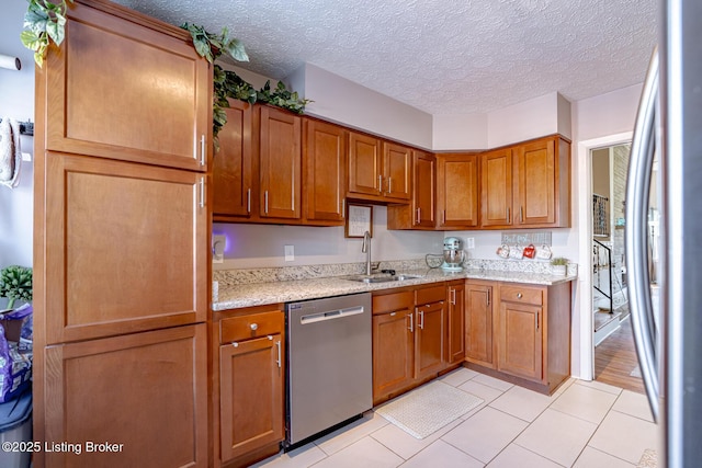 kitchen featuring sink, appliances with stainless steel finishes, light stone countertops, a textured ceiling, and light tile patterned flooring