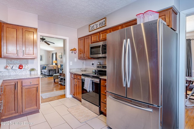 kitchen featuring light tile patterned floors, ceiling fan, appliances with stainless steel finishes, light stone countertops, and a textured ceiling