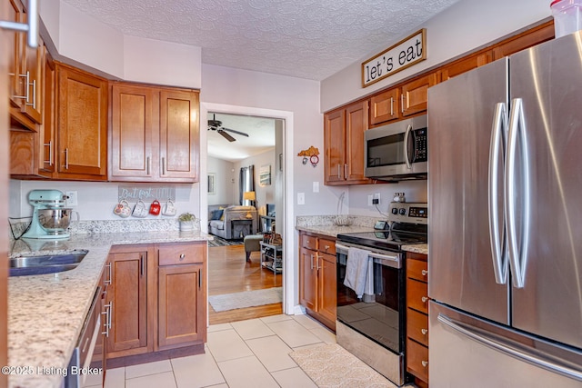 kitchen featuring ceiling fan, appliances with stainless steel finishes, light stone countertops, a textured ceiling, and light tile patterned flooring