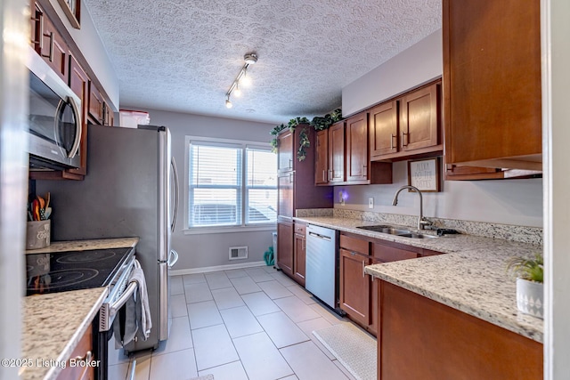 kitchen with appliances with stainless steel finishes, sink, light stone counters, track lighting, and a textured ceiling