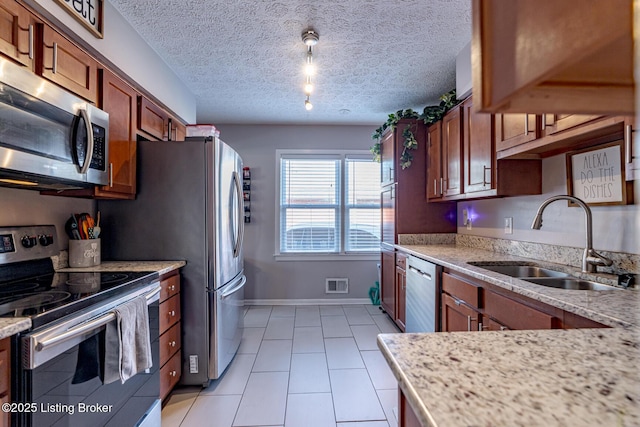 kitchen with light stone counters, sink, stainless steel appliances, and a textured ceiling