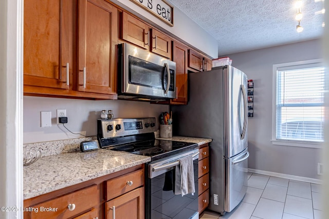 kitchen featuring stainless steel appliances, light tile patterned floors, a textured ceiling, and light stone counters