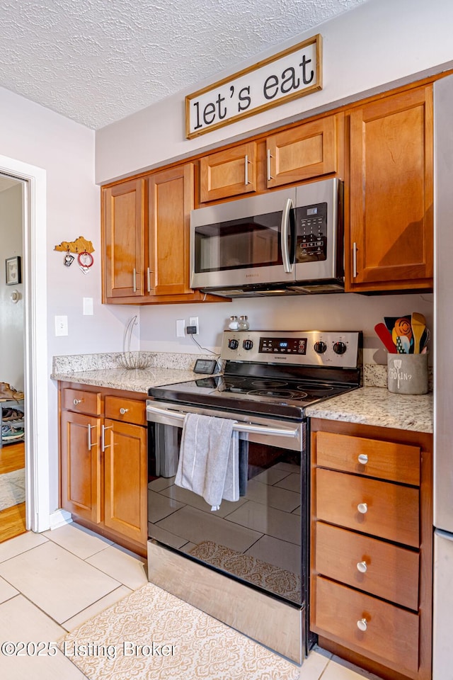 kitchen with light stone countertops, stainless steel appliances, a textured ceiling, and light tile patterned flooring