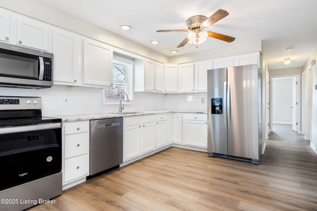 kitchen featuring sink, light wood-type flooring, stainless steel appliances, light stone countertops, and white cabinets