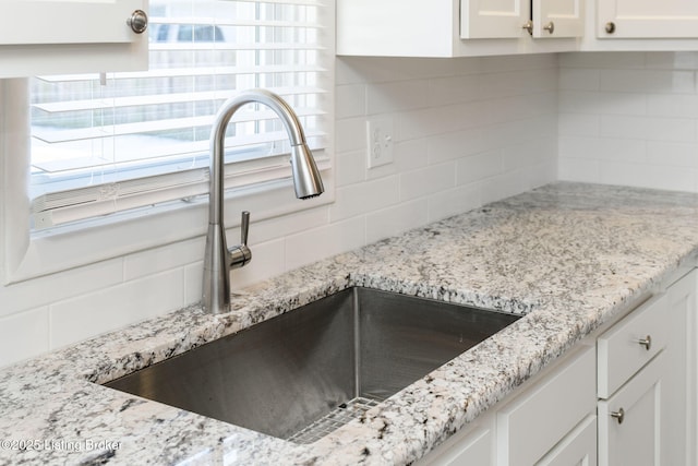 details featuring tasteful backsplash, white cabinetry, light stone countertops, and sink