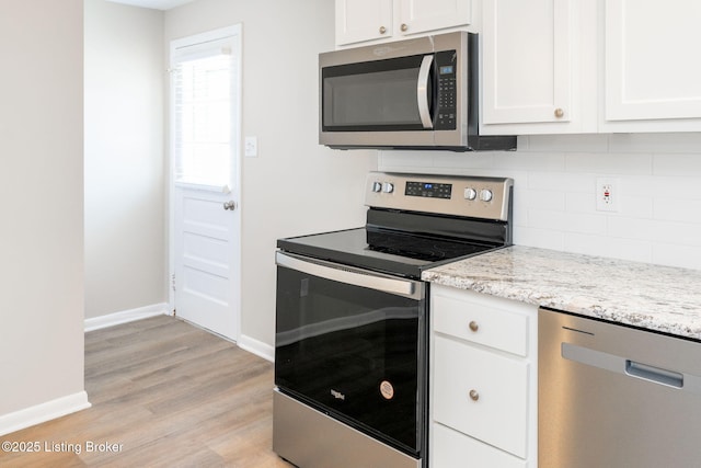 kitchen with light stone countertops, white cabinetry, appliances with stainless steel finishes, and light wood-type flooring