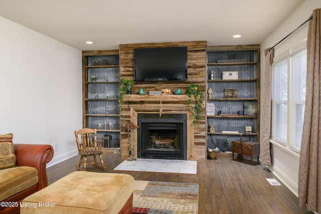 living room featuring wood-type flooring, a fireplace, and built in features