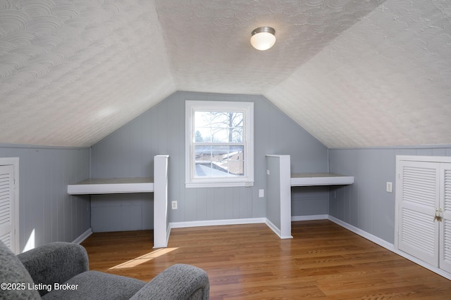 additional living space featuring lofted ceiling, wood-type flooring, and a textured ceiling