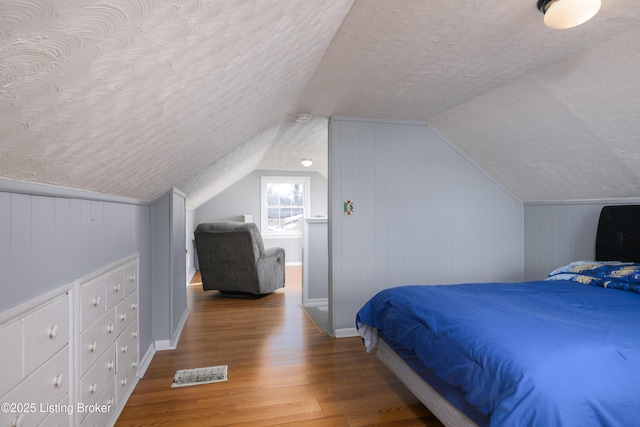 bedroom featuring vaulted ceiling, hardwood / wood-style floors, and a textured ceiling