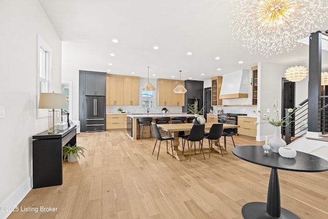 kitchen with light brown cabinetry, custom range hood, an inviting chandelier, and range with two ovens