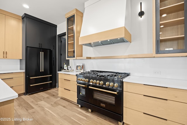 kitchen featuring high end appliances, light wood-type flooring, custom exhaust hood, and light brown cabinets