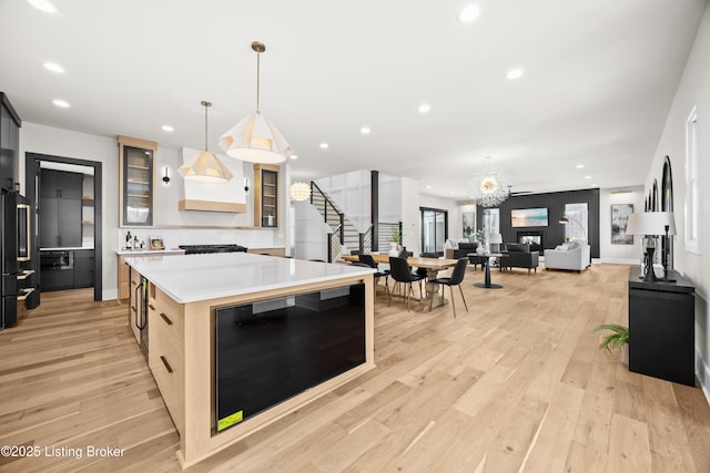 kitchen featuring a kitchen island, decorative light fixtures, beverage cooler, light brown cabinets, and light wood-type flooring