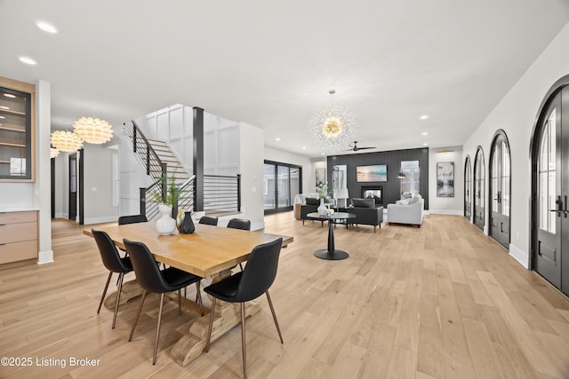 dining space featuring ceiling fan with notable chandelier, a fireplace, french doors, and light wood-type flooring