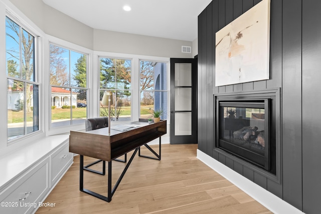 home office with a large fireplace and light hardwood / wood-style floors