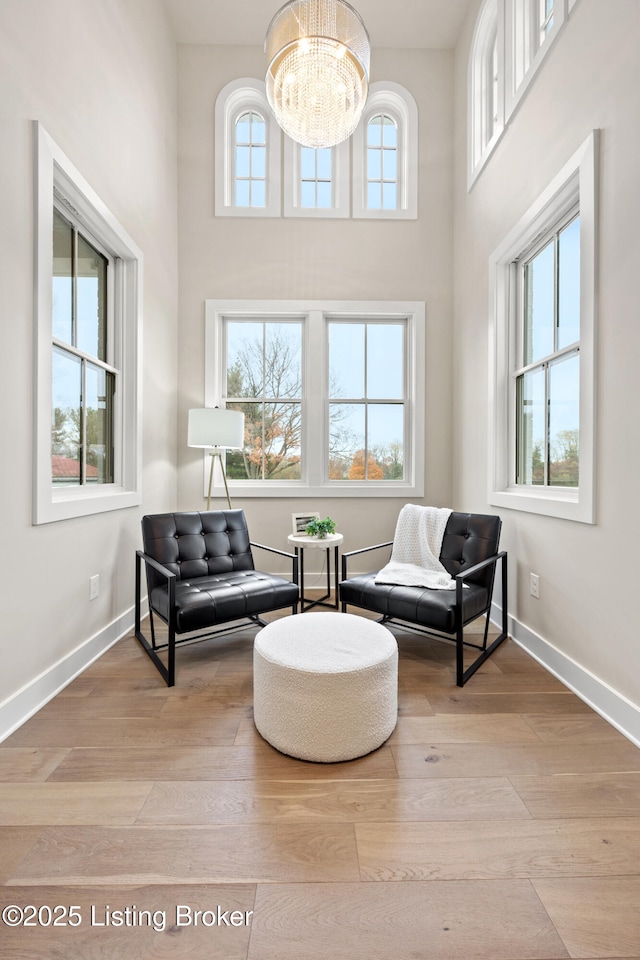 sitting room featuring an inviting chandelier, a towering ceiling, light hardwood / wood-style floors, and a healthy amount of sunlight