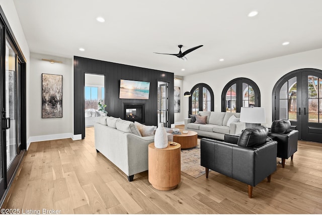 living room with french doors, a large fireplace, a healthy amount of sunlight, and light hardwood / wood-style flooring