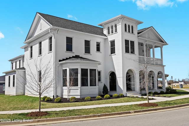 view of front of home with a balcony, a front lawn, and roof with shingles